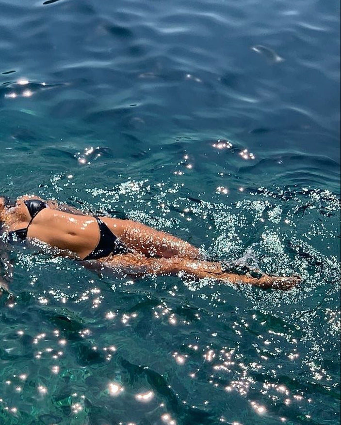Person swimming in clear blue water with sunlight reflecting off the surface